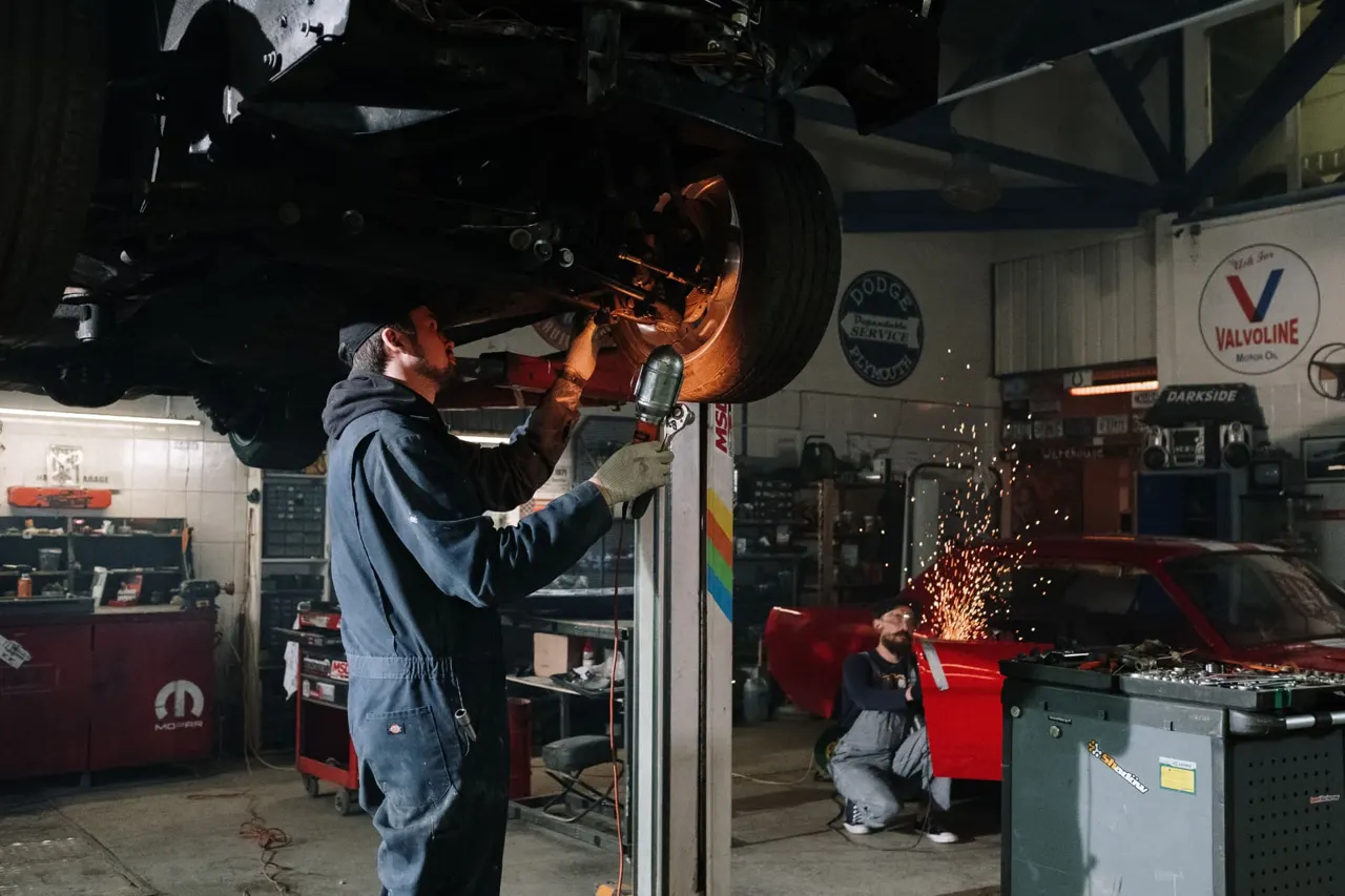 Technician working under a lifted car in a busy auto repair shop